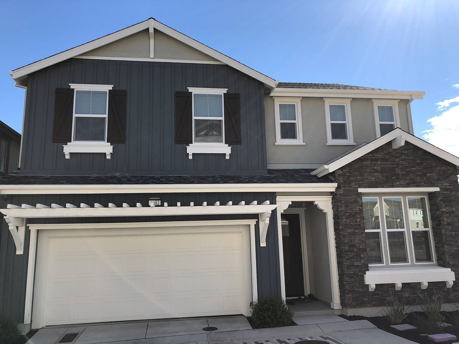 Two-story house with dark blue siding, stone accents, and a white garage door against a blue sky.