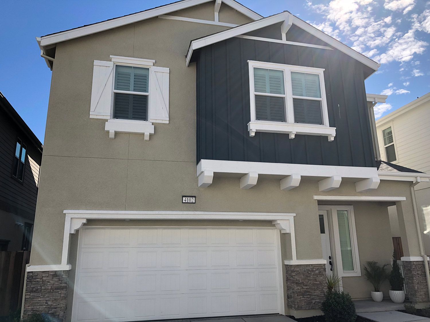 Two-story house with tan stucco exterior, white trim, blue siding accent, and a white garage door.