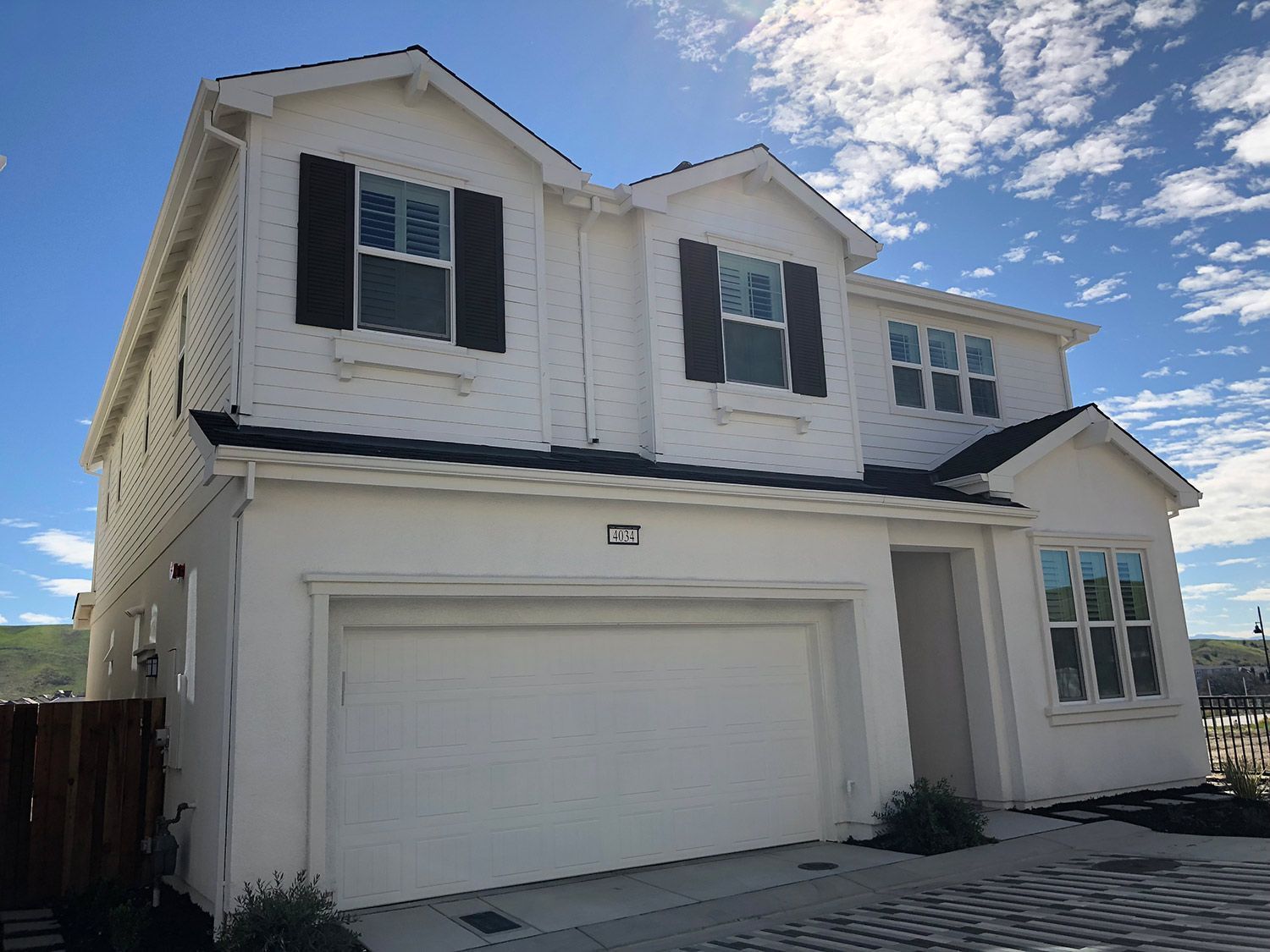 Two-story white house with black shutters, attached garage, blue sky, and patchy clouds.