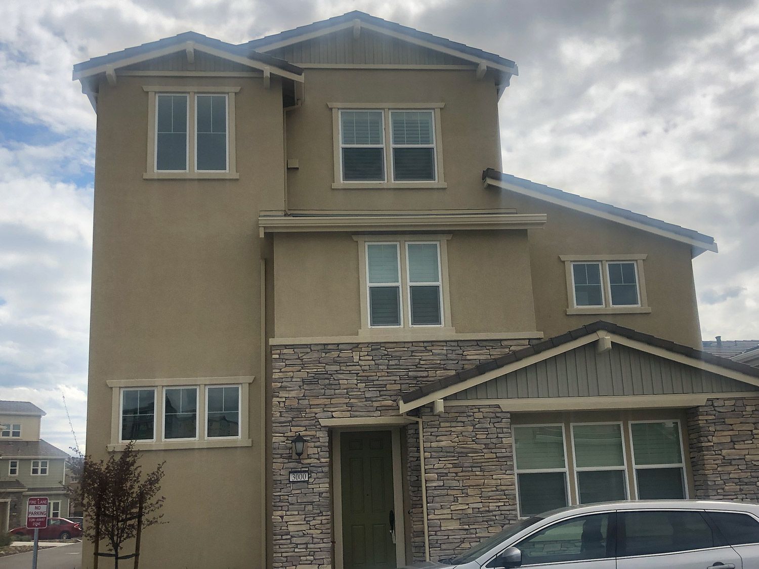 Three-story house with stone veneer on the bottom. Beige stucco siding with white trim. Cloudy sky.