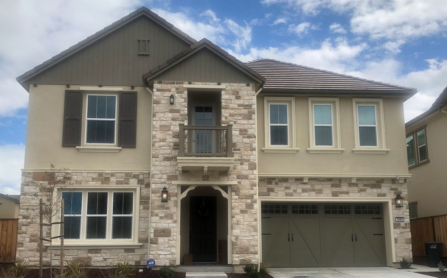 Two-story house with stone and stucco facade, brown trim, and a three-car garage under a cloudy sky.