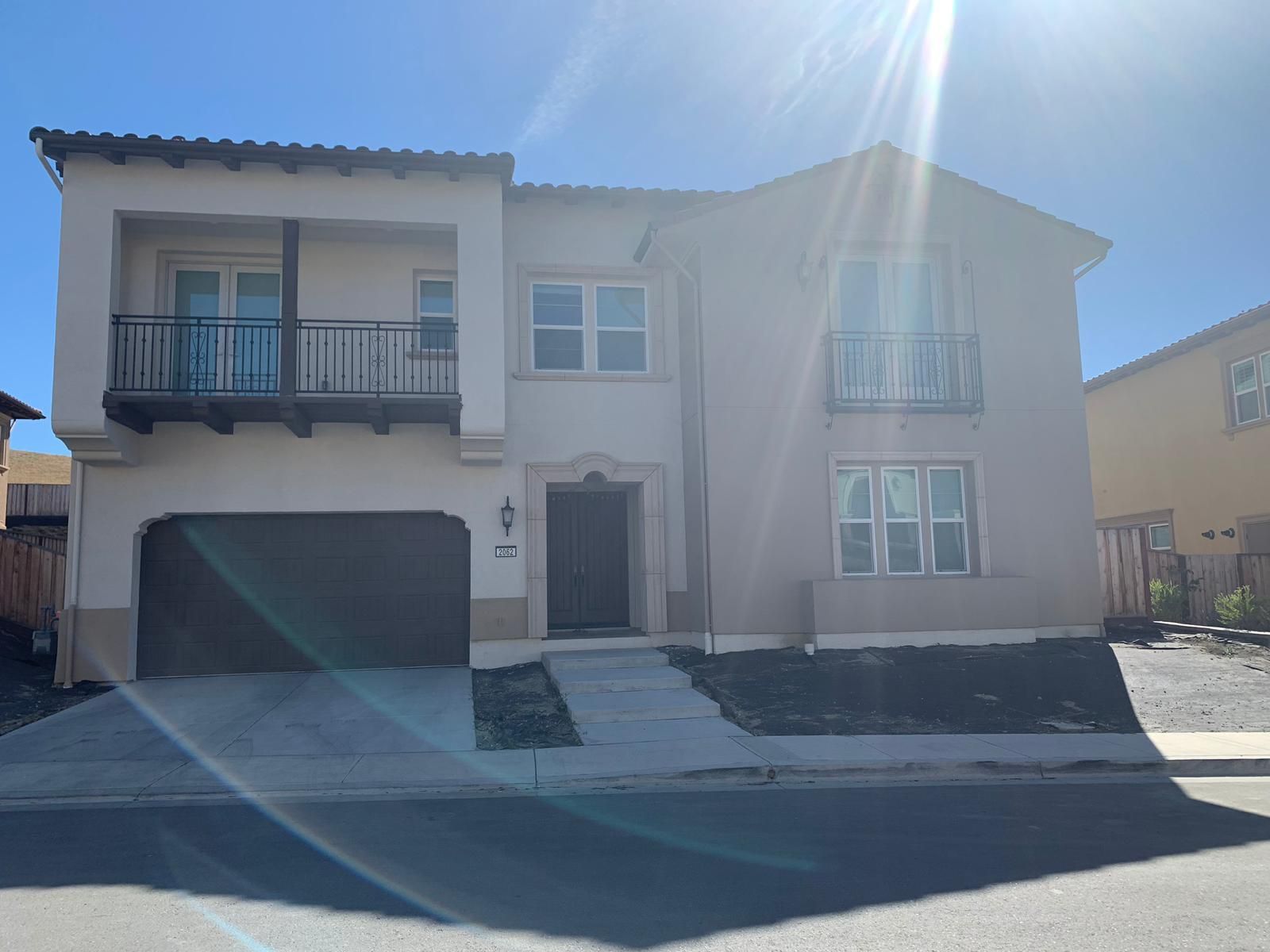 Two-story stucco house with balcony and garage on a sunny day.