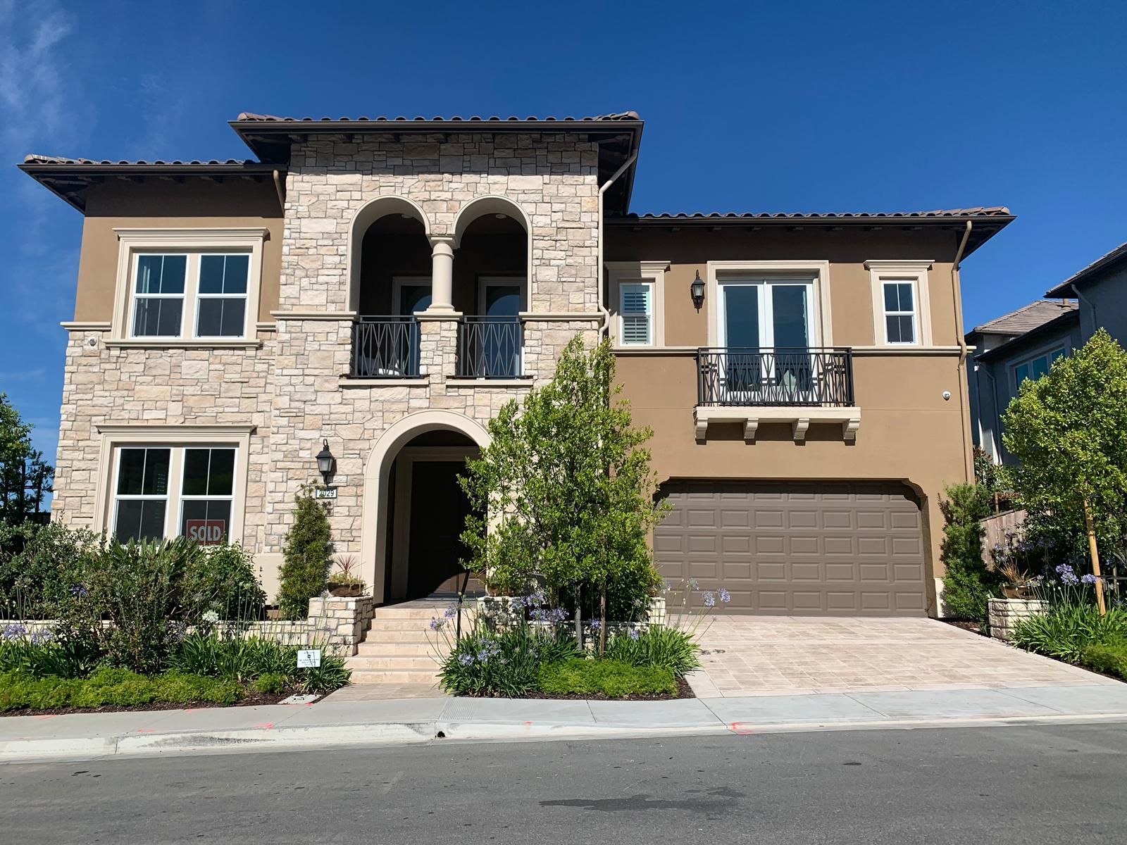 Two-story stucco house with stone facade, arched entryway and balcony, beige garage door, and landscaping.