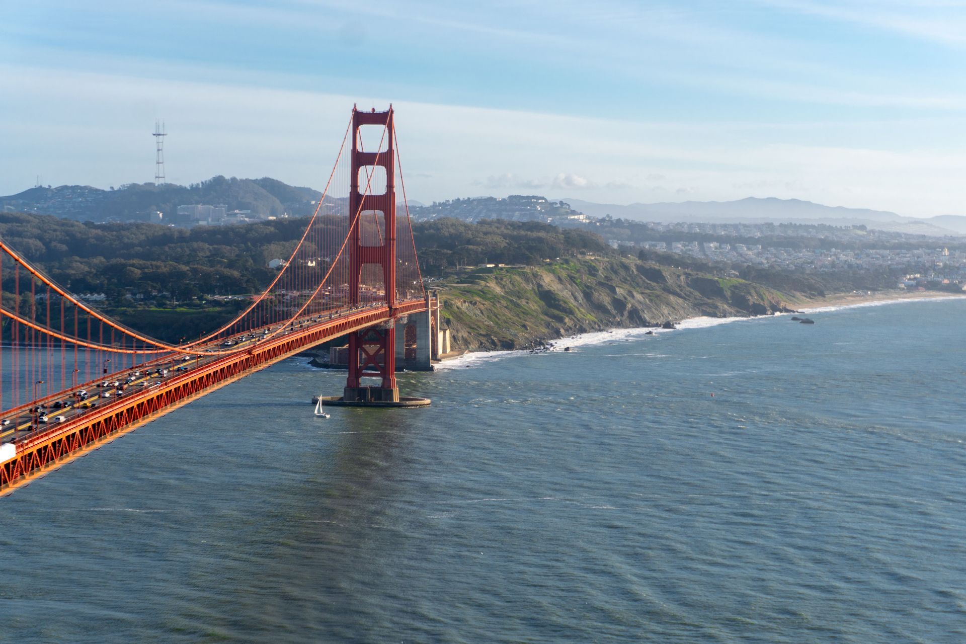 Golden Gate Bridge stretching over blue water with the red tower and hazy coastline in the distance