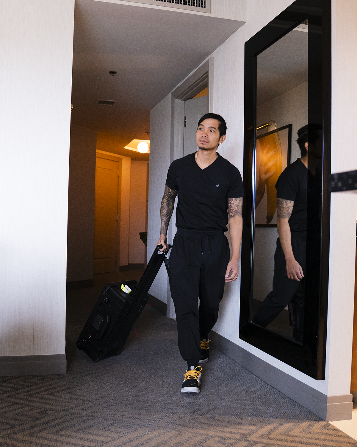 Person in black outfit pulls a suitcase down a hotel hallway.