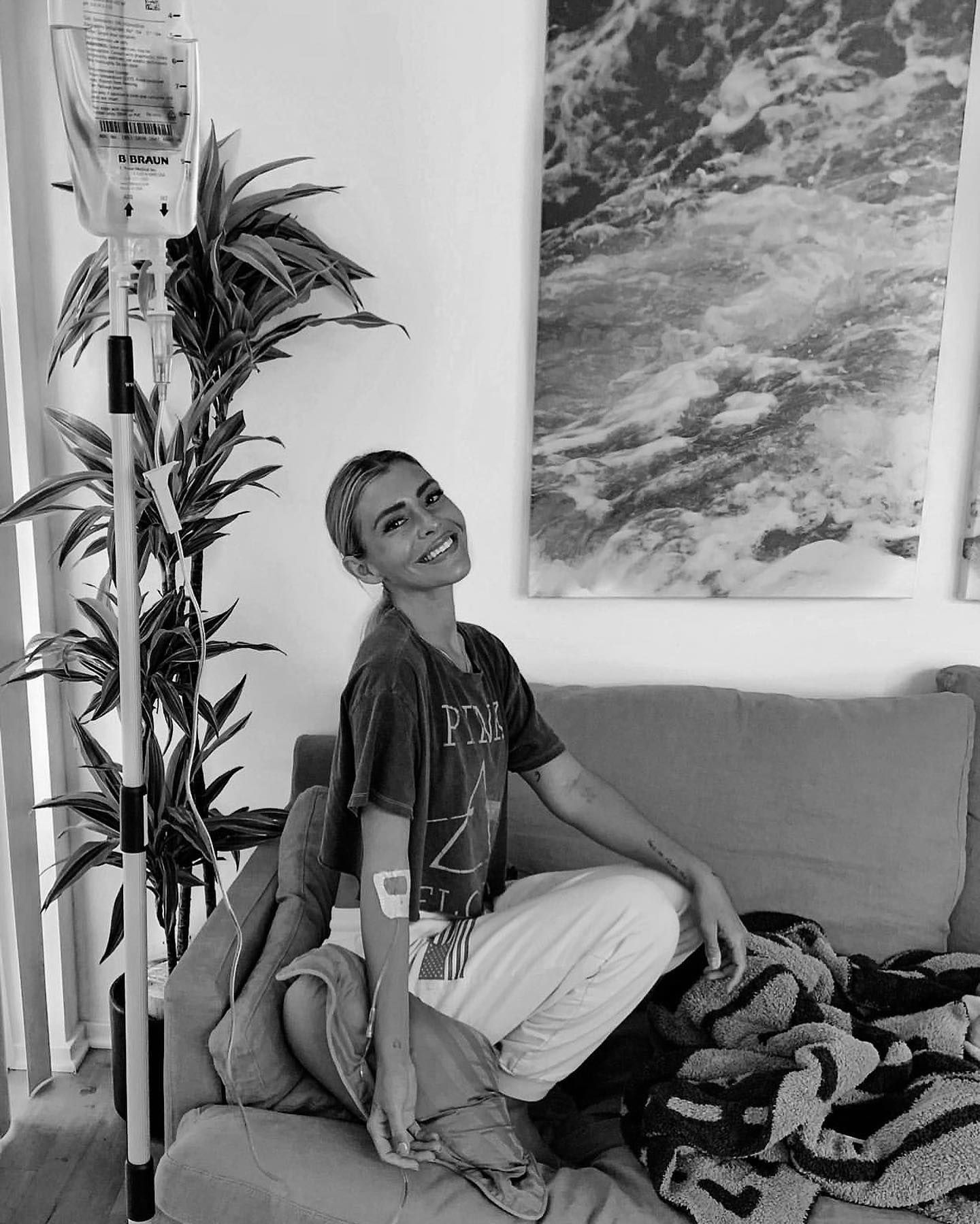 Person smiling on a couch beside a tall plant and abstract wall art in a black-and-white room.