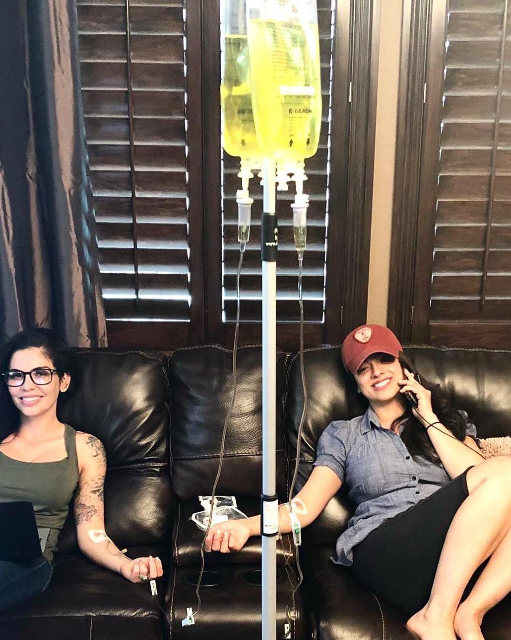 Two people relaxing on a couch beside an IV stand in a dim room