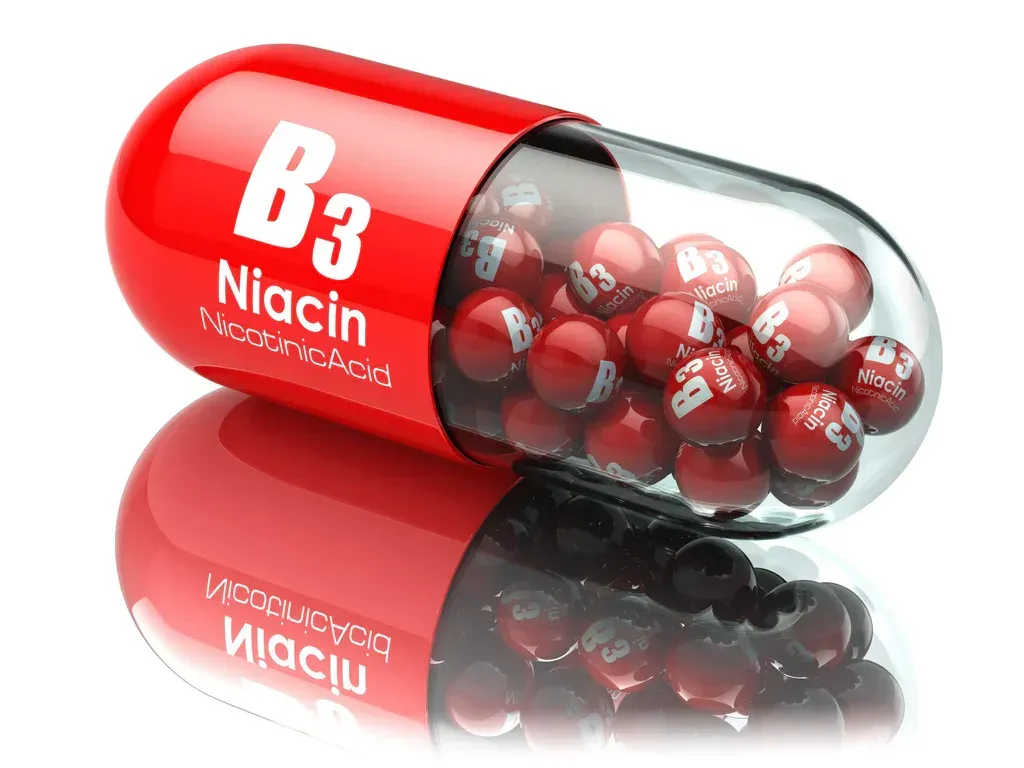 Red B3 niacin capsule spilling red tablets on a reflective white background