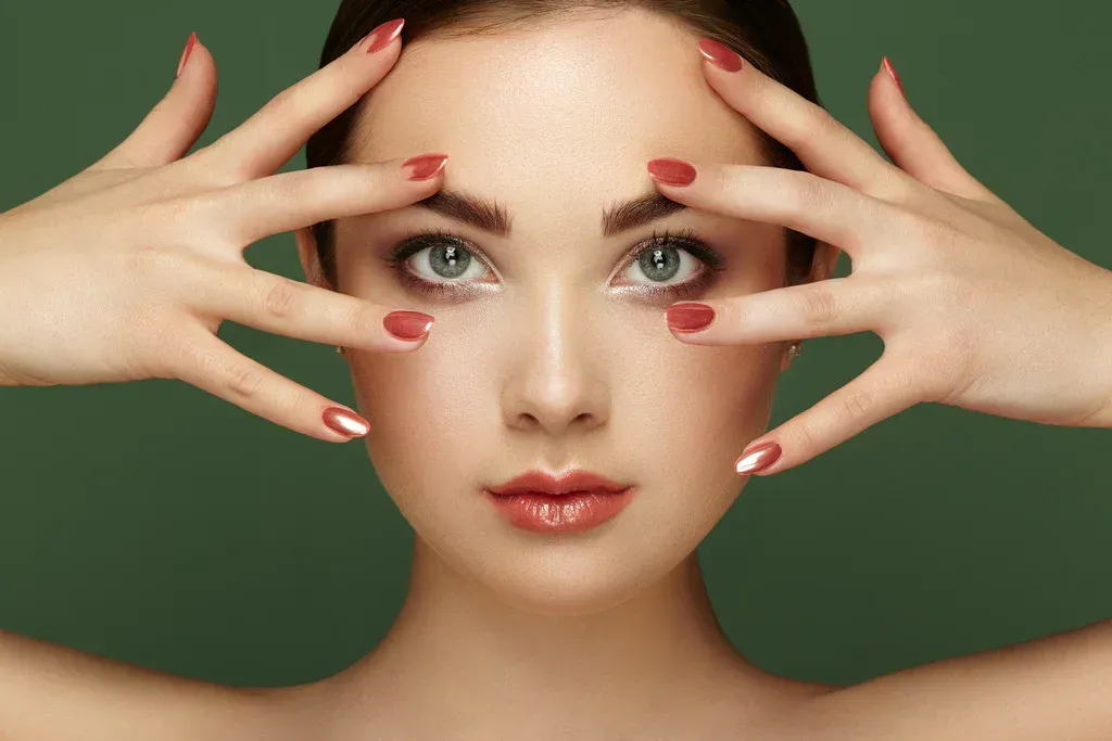 Woman with red-painted nails framing her face against a green background