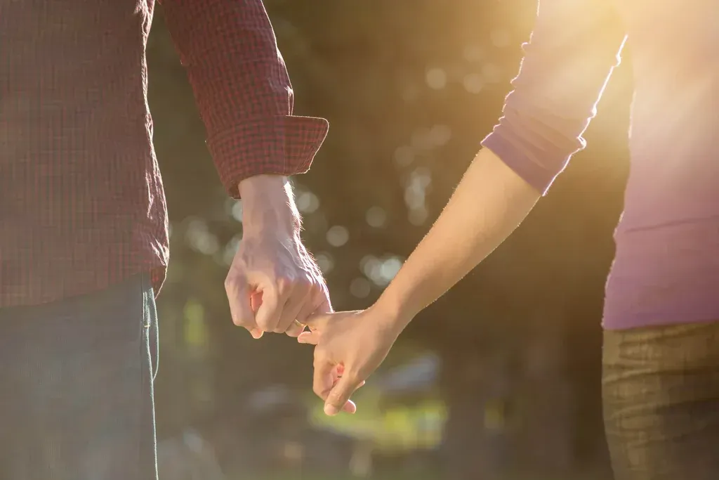 Two people holding hands outdoors in warm sunlight
