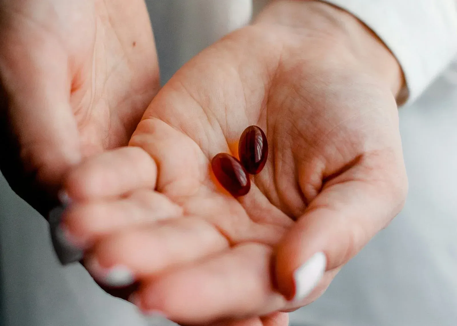 Open hands holding two dark red capsules