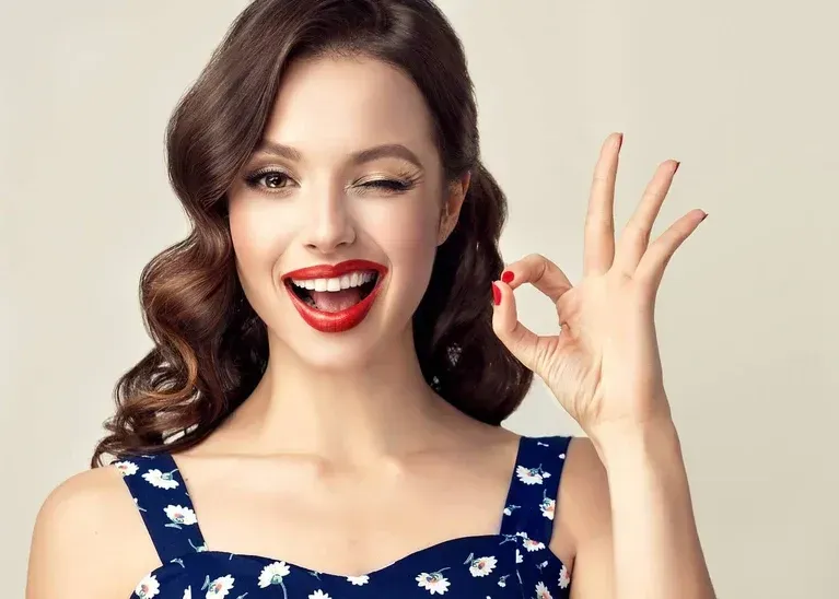 Smiling woman in a blue floral dress making an OK hand gesture