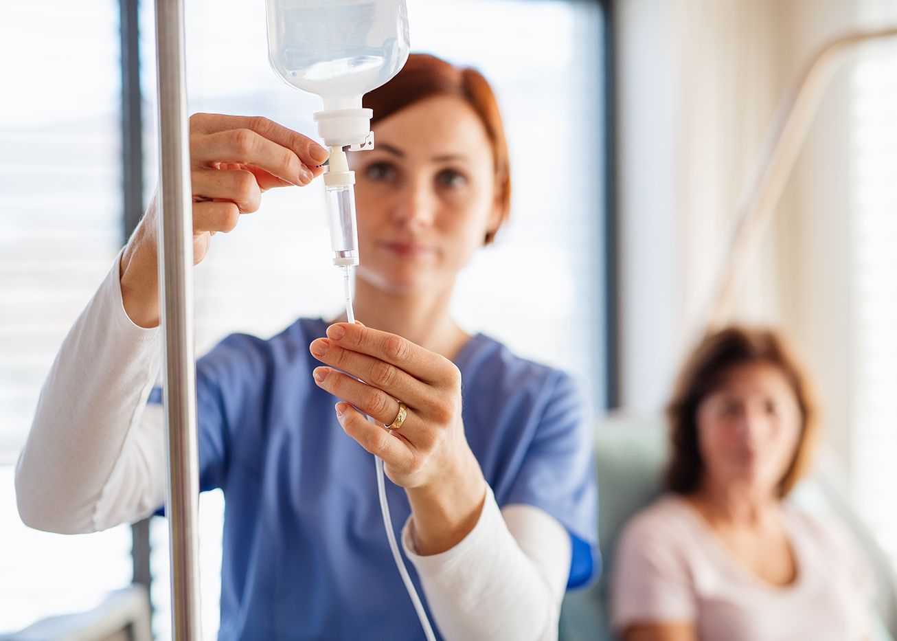 Nurse adjusting IV drip beside a patient in a hospital room