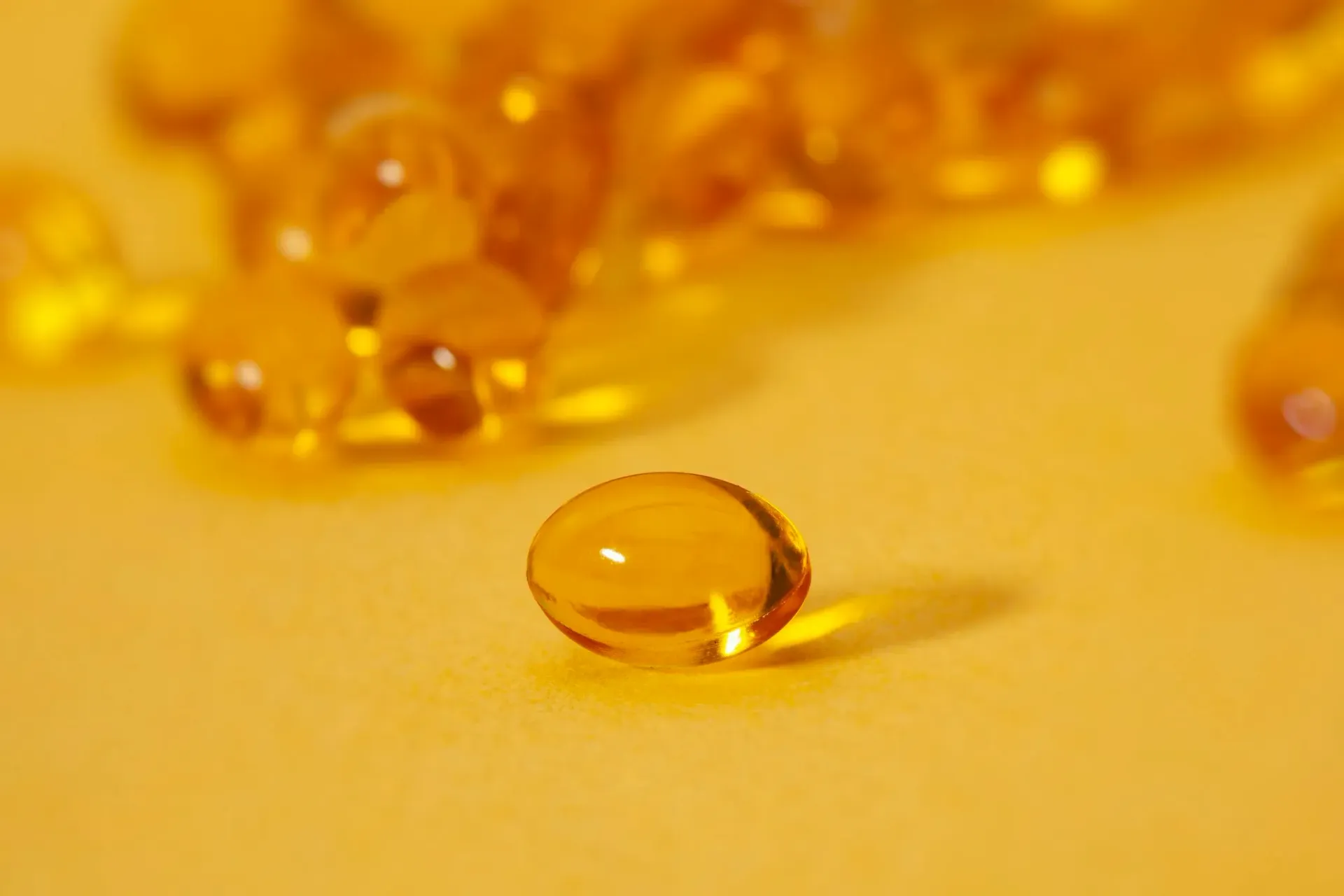 Transparent amber droplets on a yellow surface, with one drop in sharp focus.