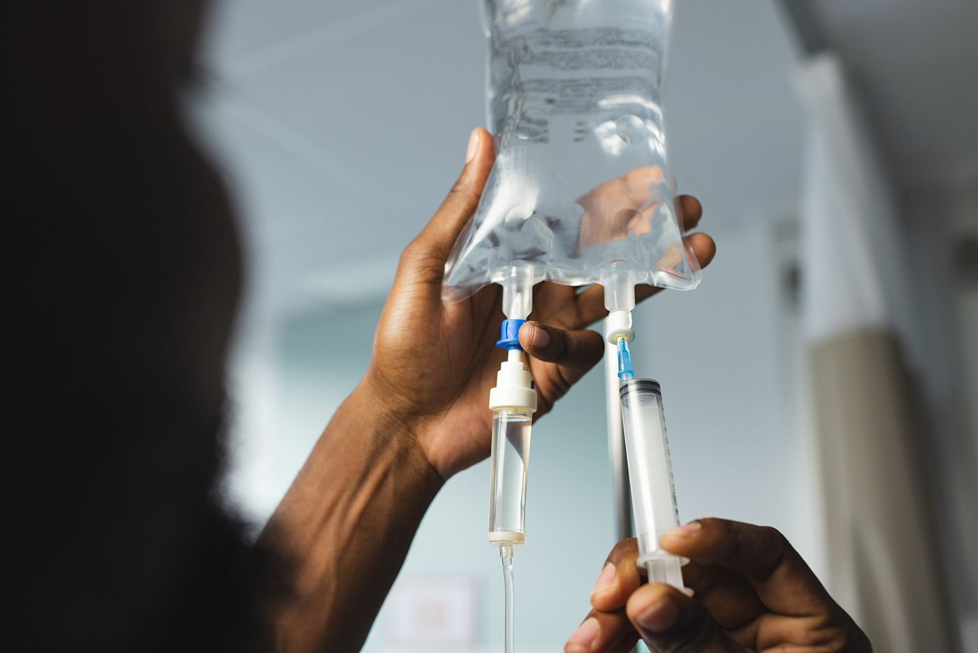 Hands connect IV tubing to an inverted clear bottle, likely preparing an infusion.