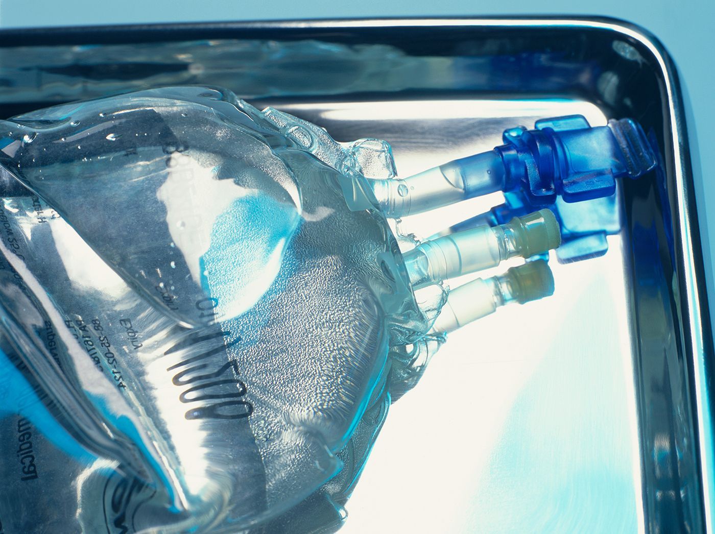 Close-up of a clear plastic medical tube with blue connectors and liquid inside inside a tray