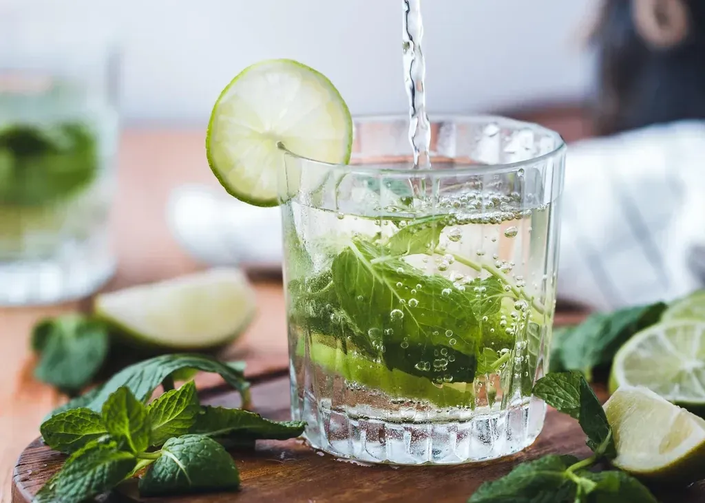 Mint mojito in a glass with lime slices and mint leaves on a wooden table, with lime wedges nearby