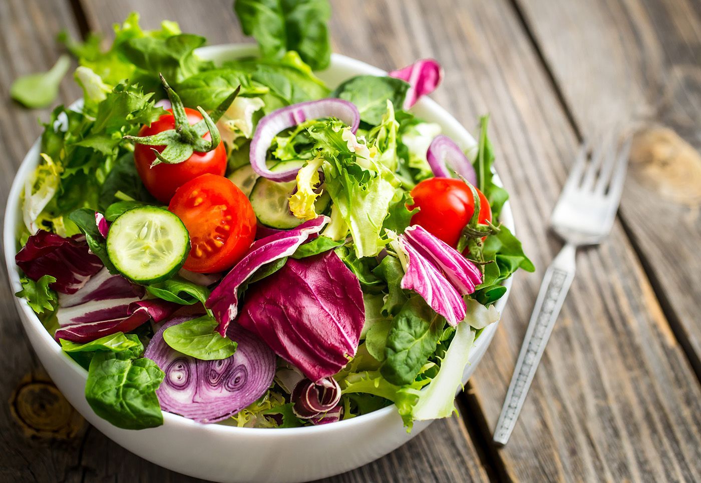 Fresh garden salad with lettuce, tomatoes, cucumber, red onion, and herbs in a bowl on a wooden table
