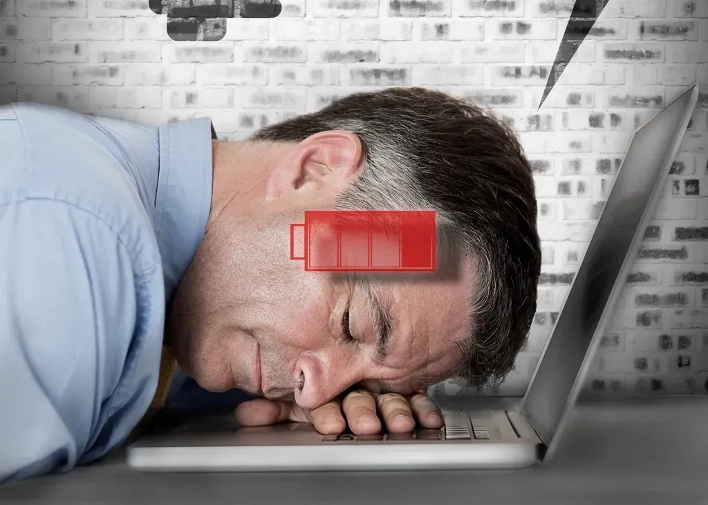 Exhausted man asleep with his head on a laptop keyboard at a desk