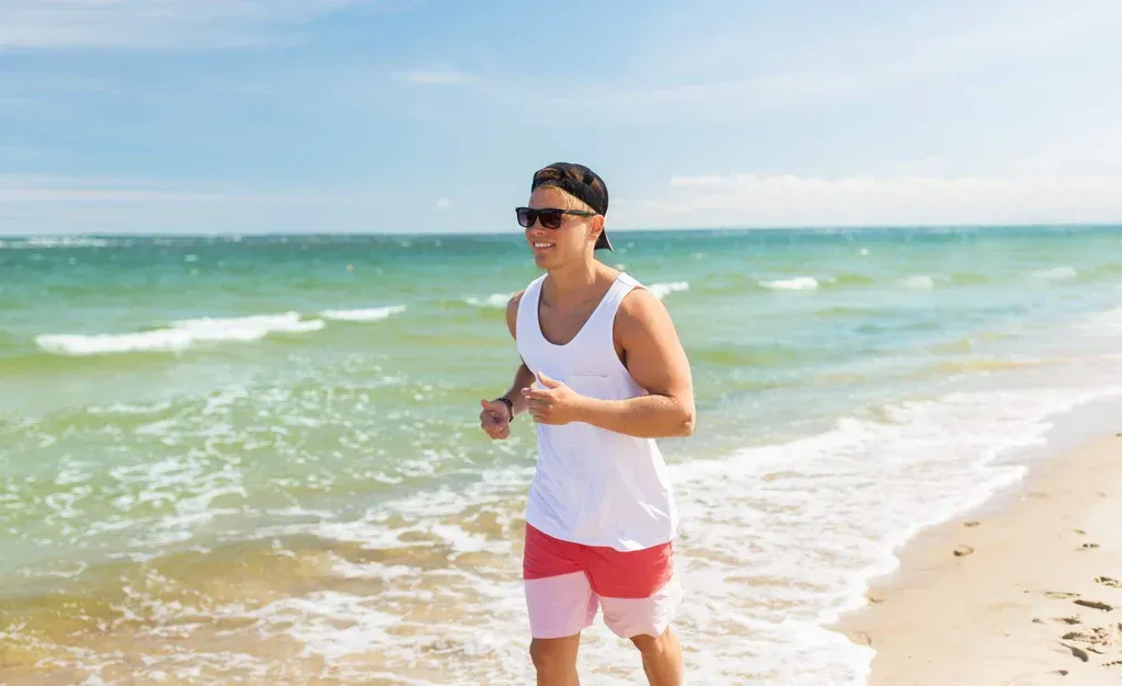 Person jogging along a sunny beach beside turquoise water.