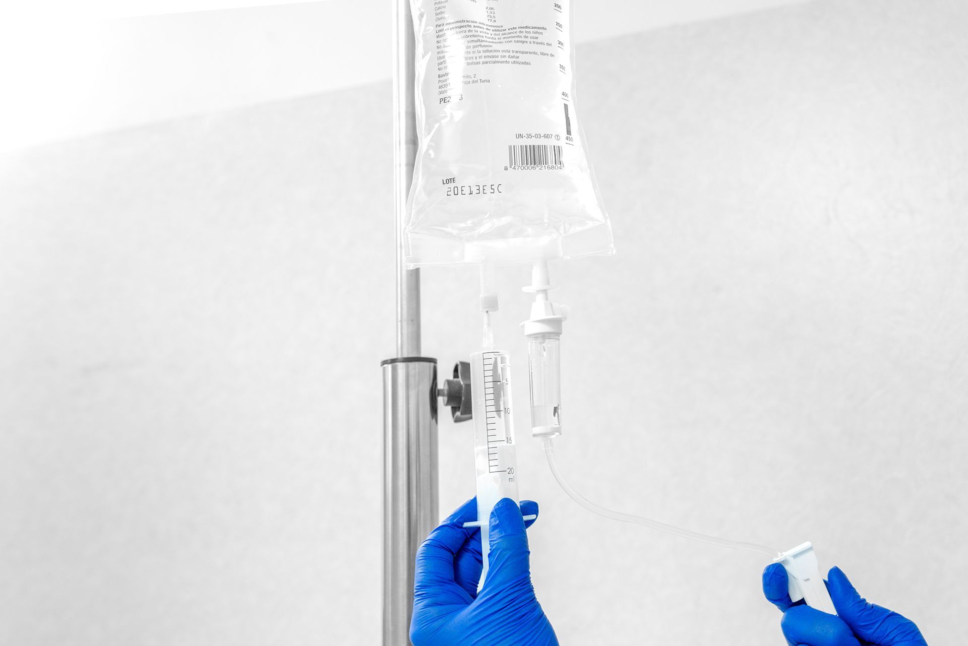 Blue-gloved hands adjusting an IV drip bag and tubing in a hospital setting