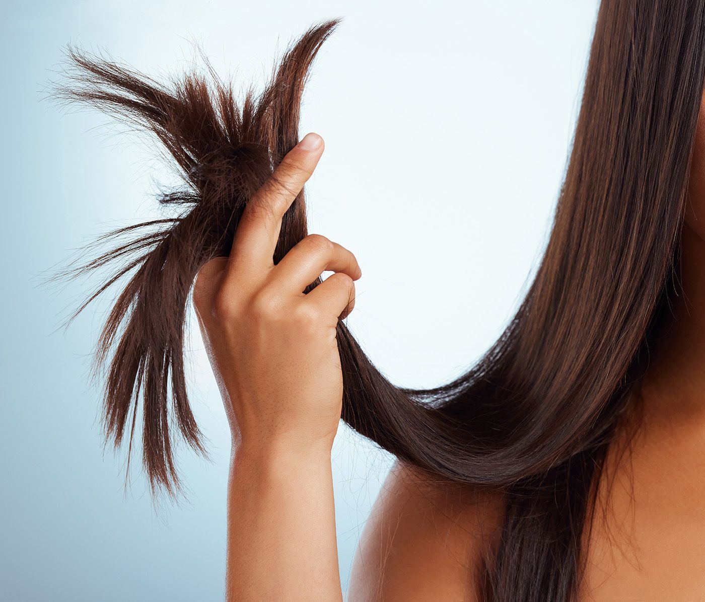 Hand holding a section of long, straight brown hair against a light background
