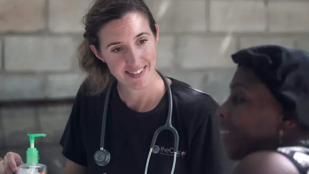 Smiling doctor with stethoscope talking to a patient at a table with hand sanitizer nearby