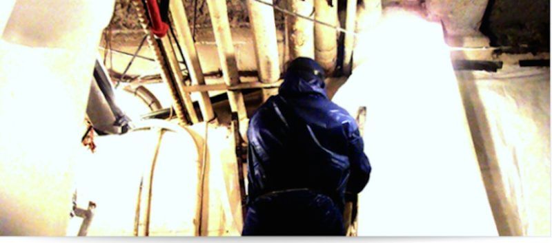 Person in blue hazmat suit inside a bright room, facing bright light.