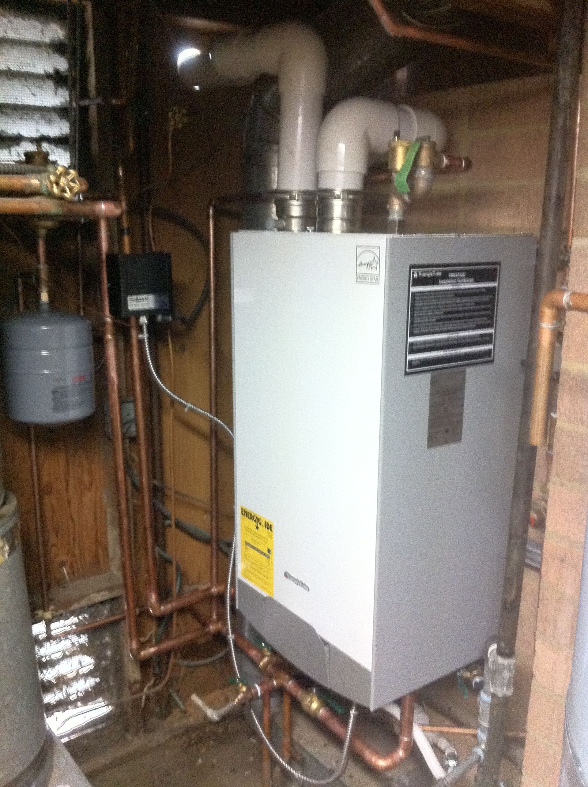 A boiler is sitting in a basement next to a water heater.