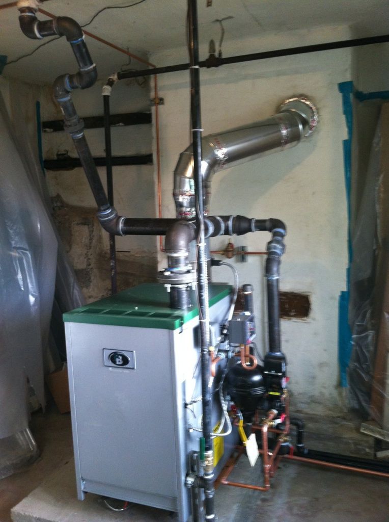 A boiler is sitting in a room with pipes coming out of it.