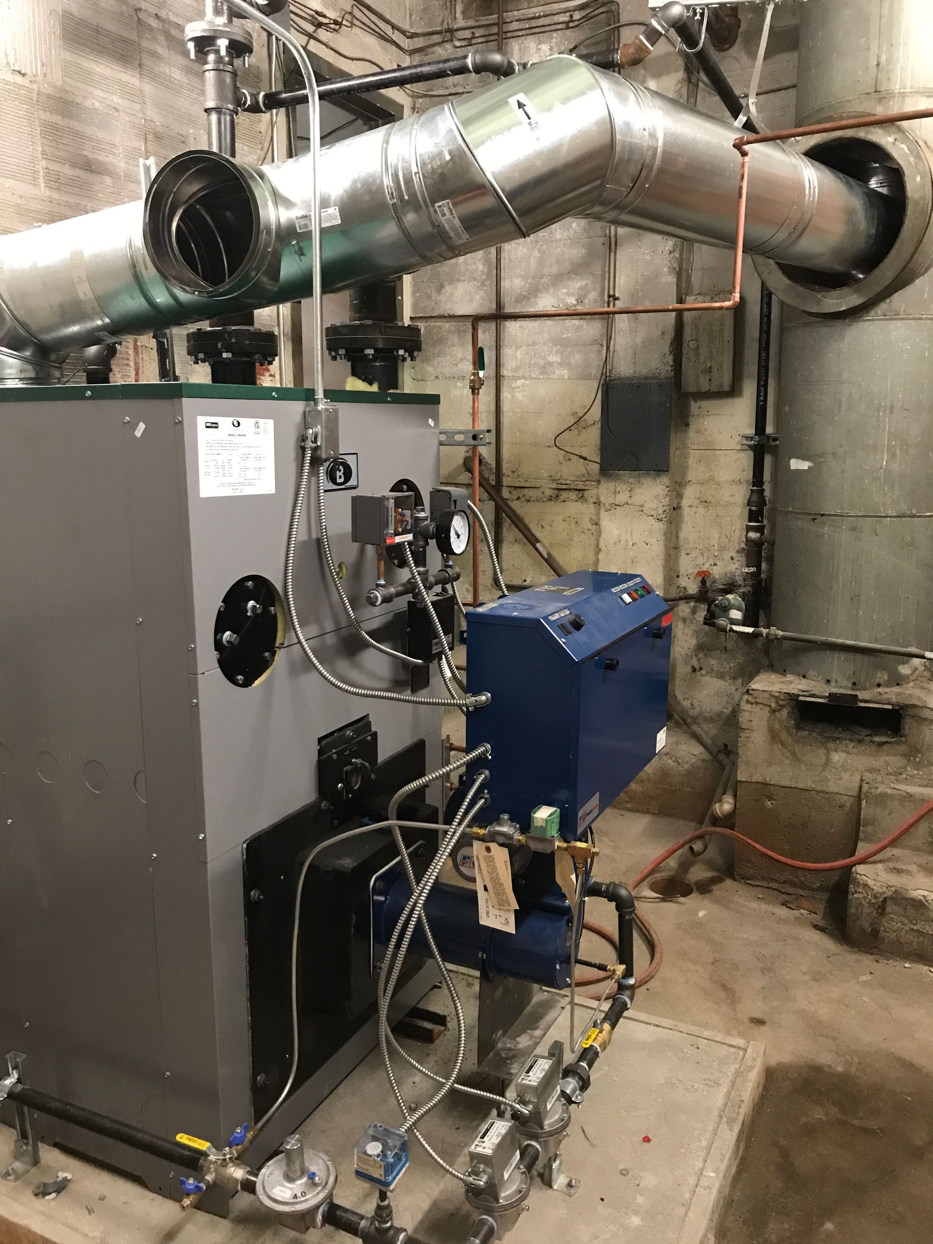 A large boiler is sitting in a room with pipes coming out of it.