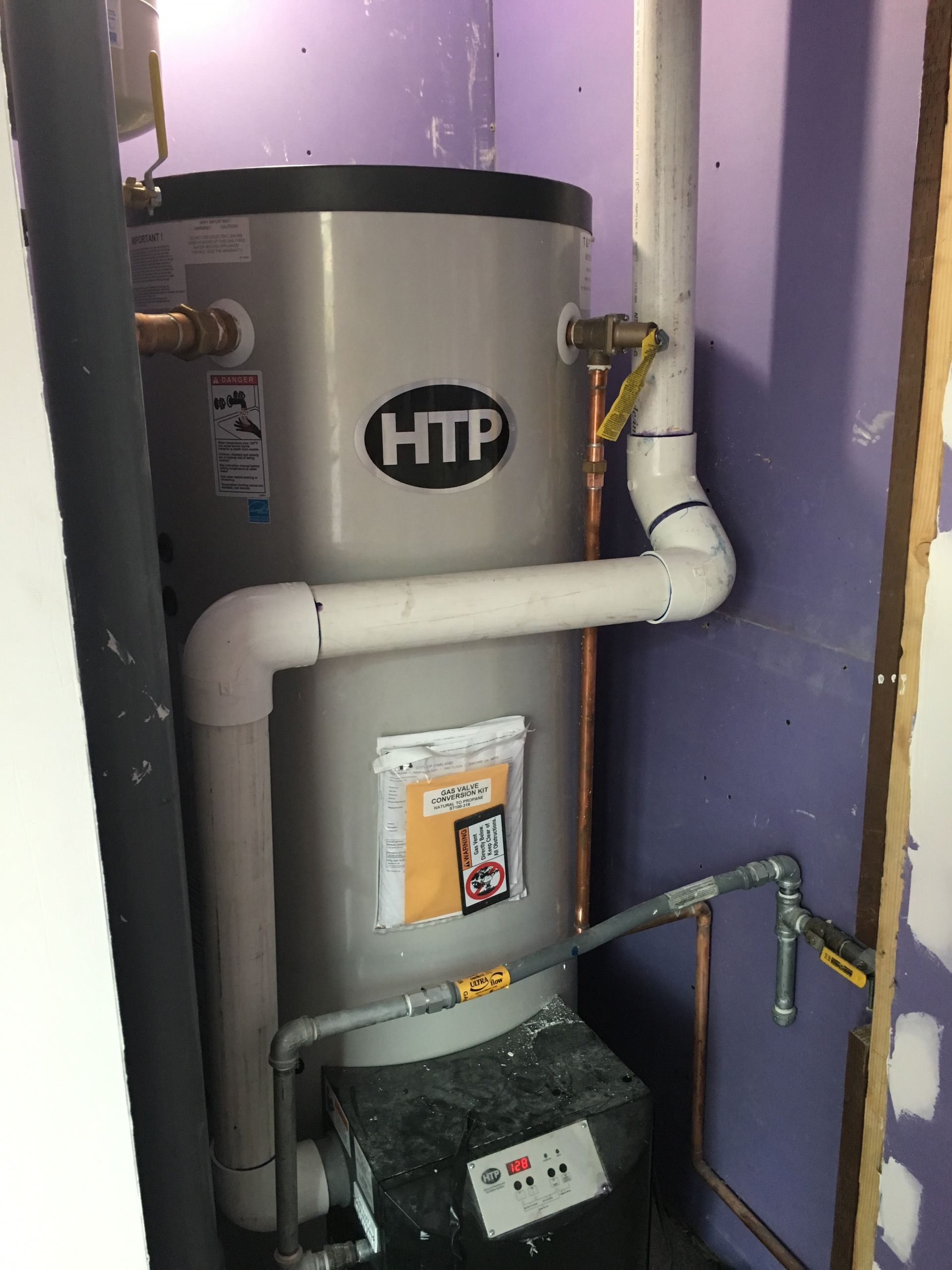 A htp water heater is sitting in a room next to a purple wall.