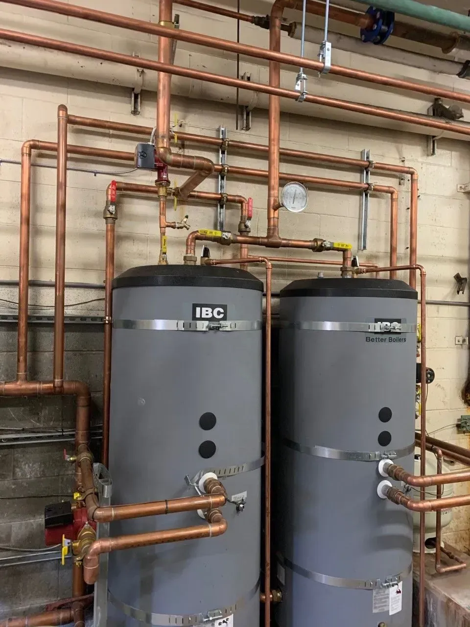 Two water heaters are connected to copper pipes in a room.