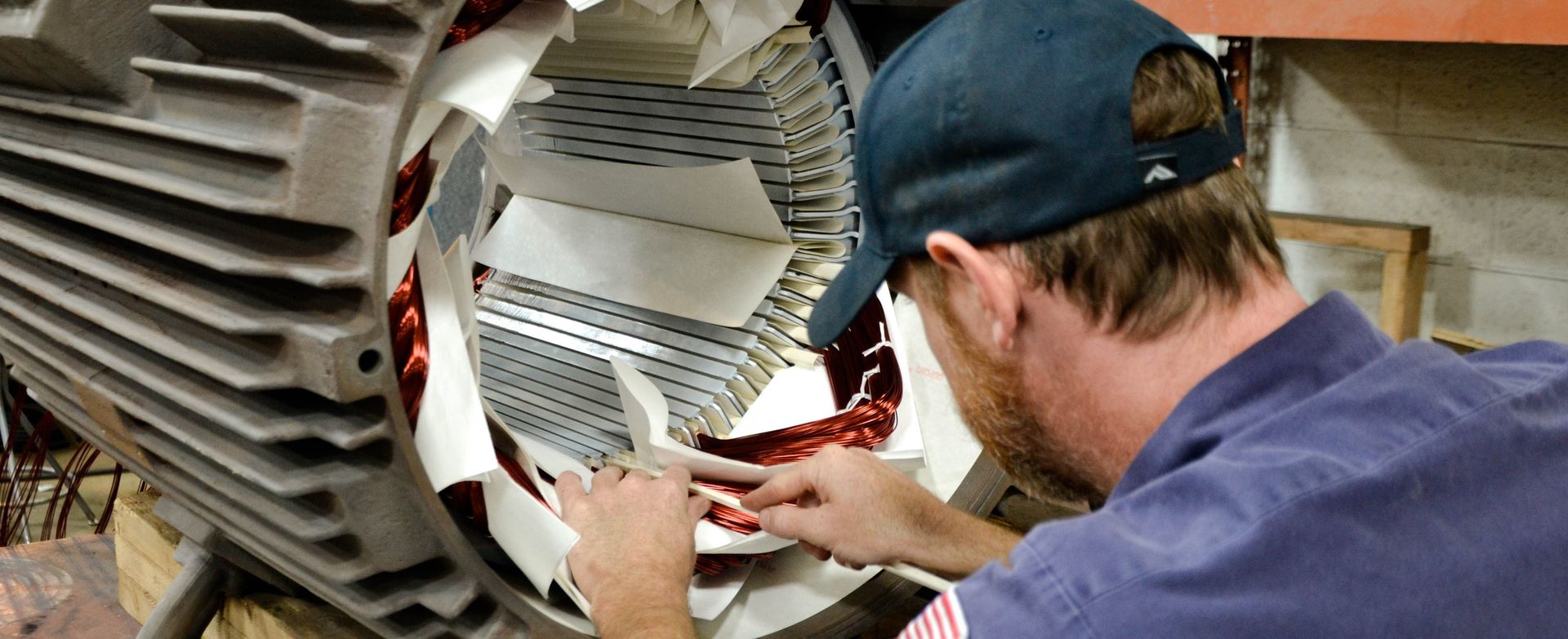 A man in a blue hat is working on an electric motor.