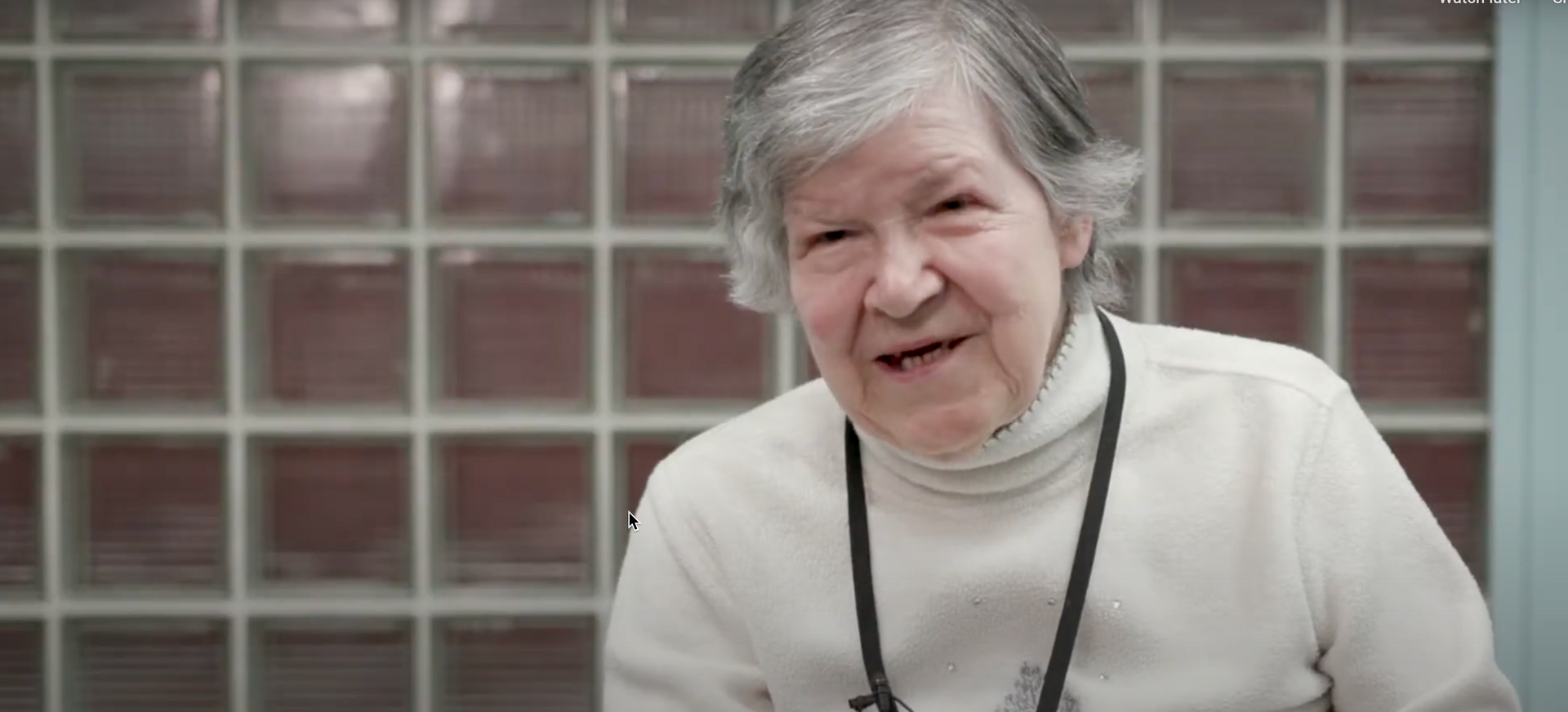 An elderly woman wearing a stethoscope around her neck is smiling.