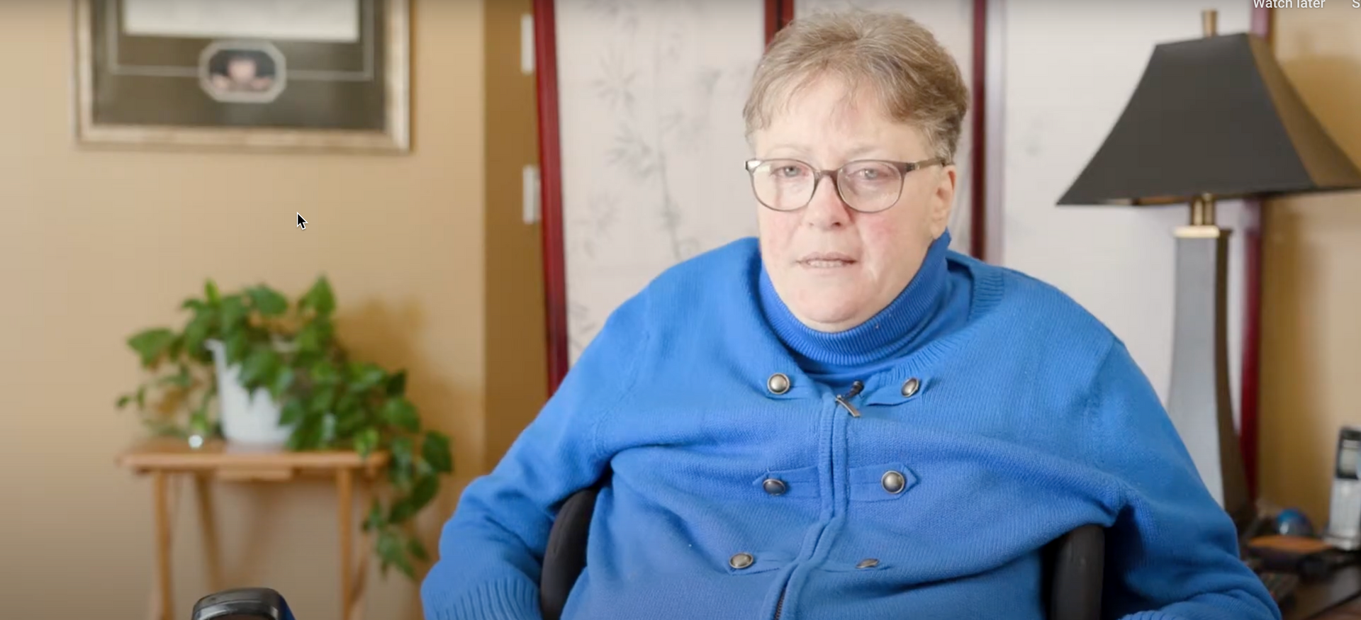 A woman in a blue sweater is sitting in a wheelchair in a living room.