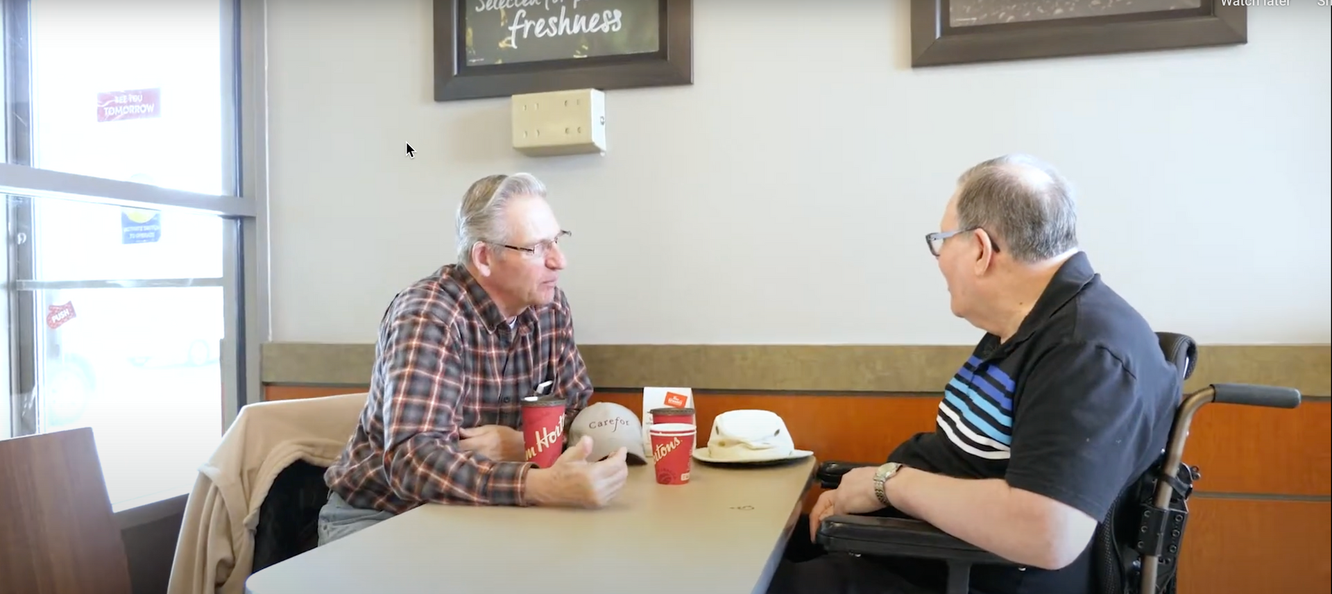 Two men are sitting at a table in a restaurant talking to each other.