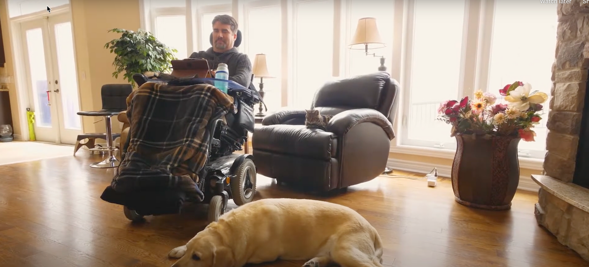 A man in a wheelchair is sitting in a living room next to a dog.