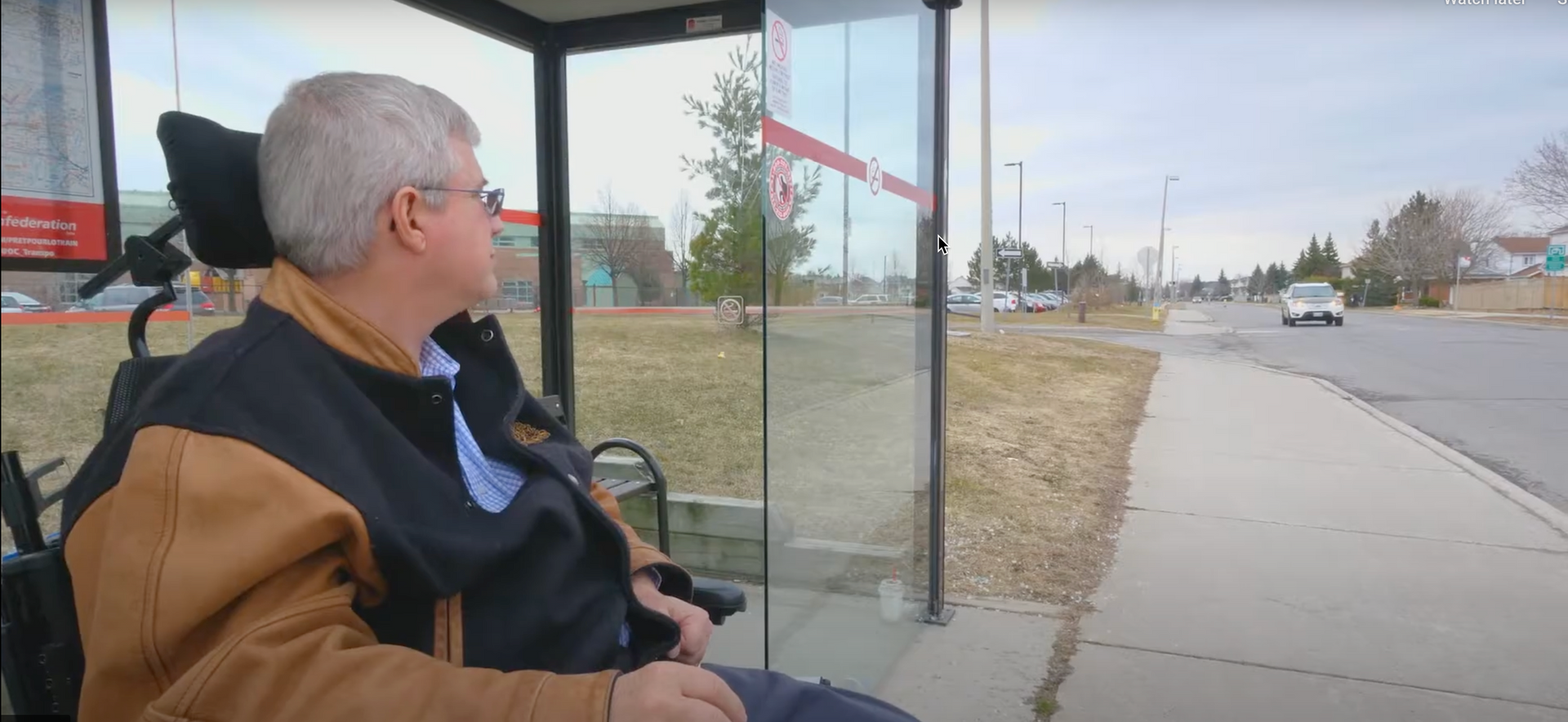 Un homme en chaise roulante est assis à un arrêt de bus.