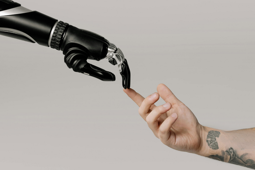 Une main robotique prothétique touchant un doigt humain. Fond gris.