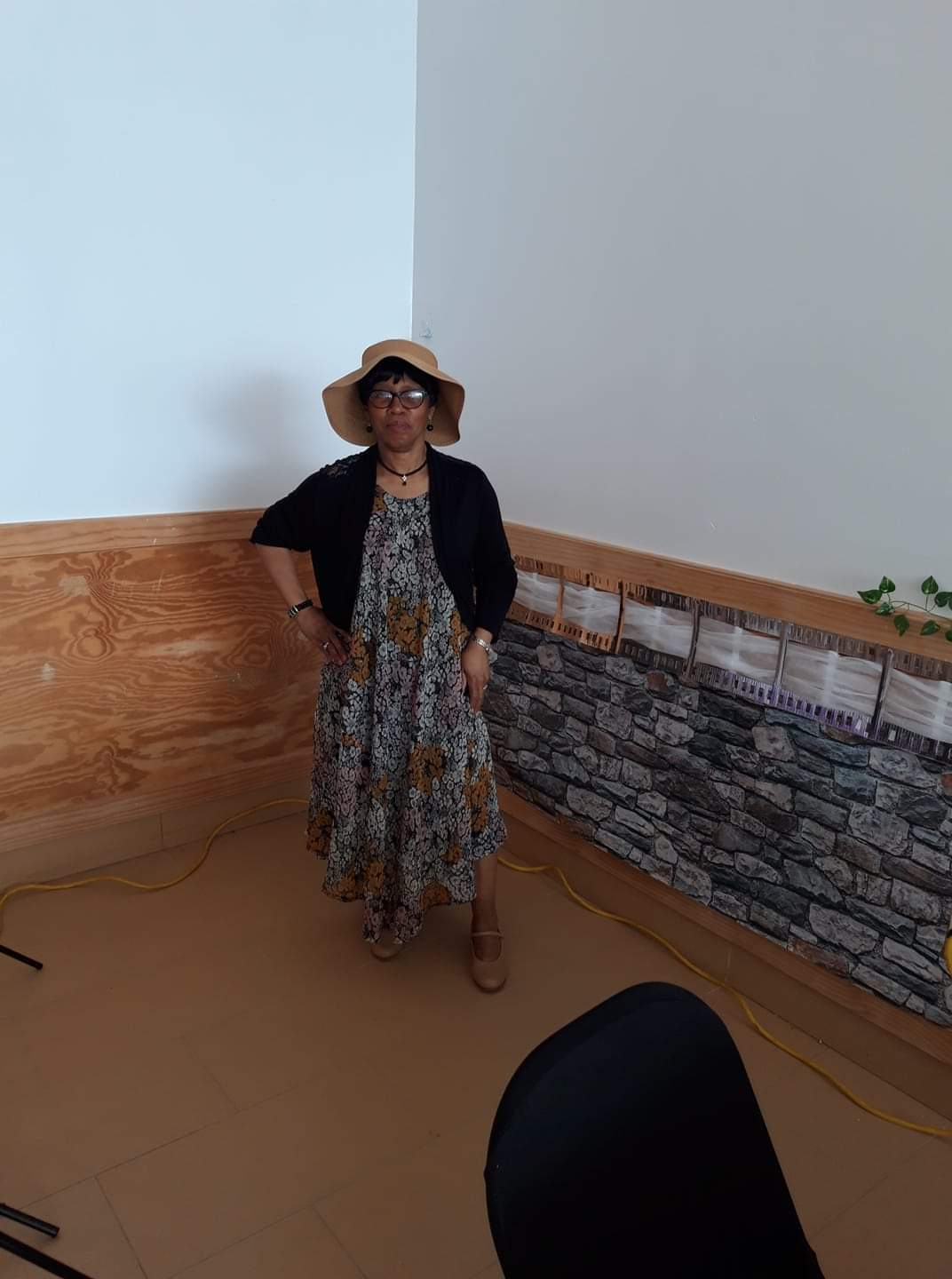 a woman in a dress and hat is standing in a corner of a room .