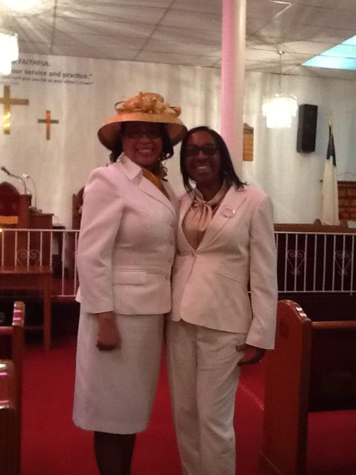 two women in white suits pose for a picture in a church