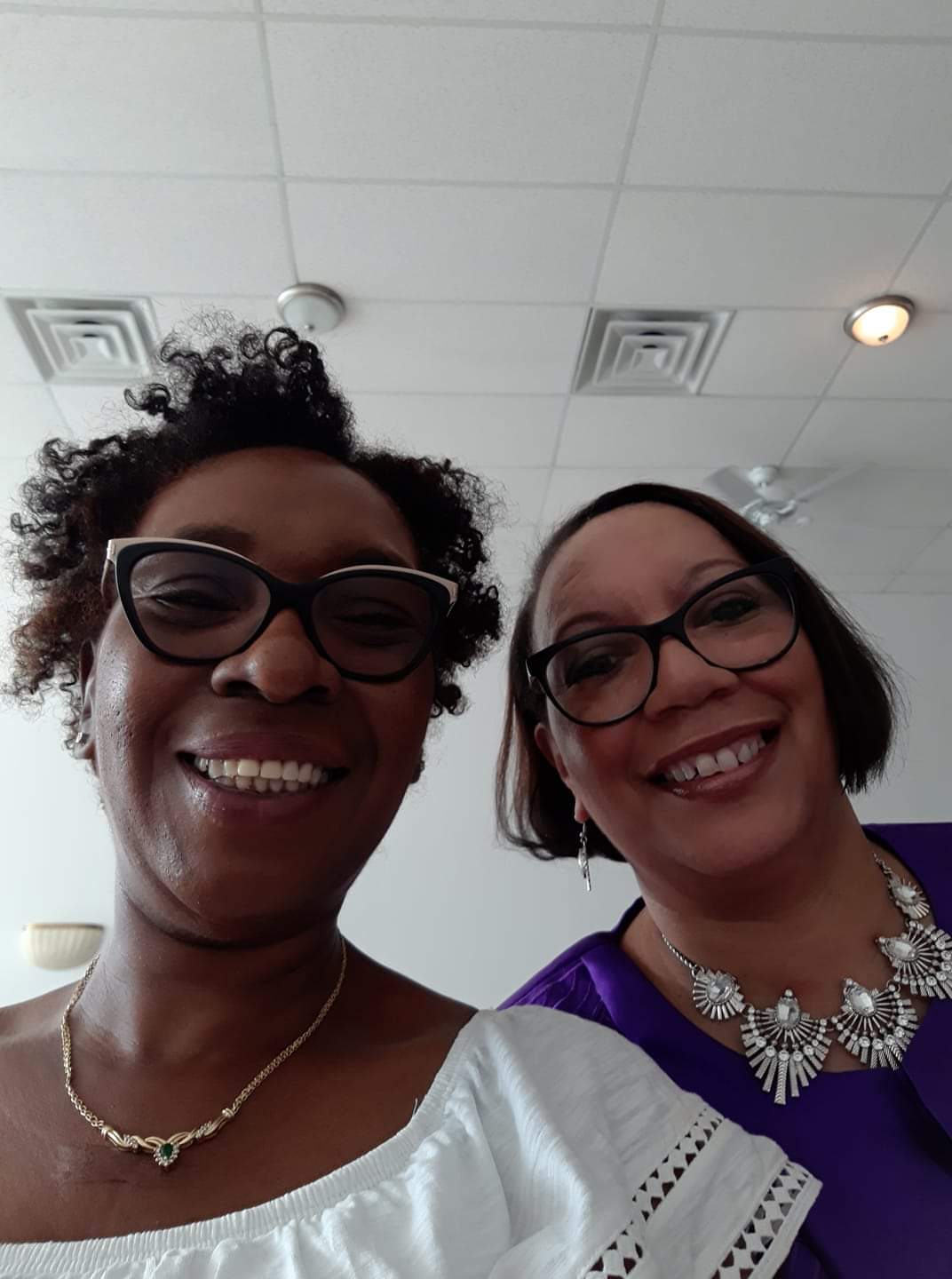 two women wearing glasses and necklaces smile for a picture