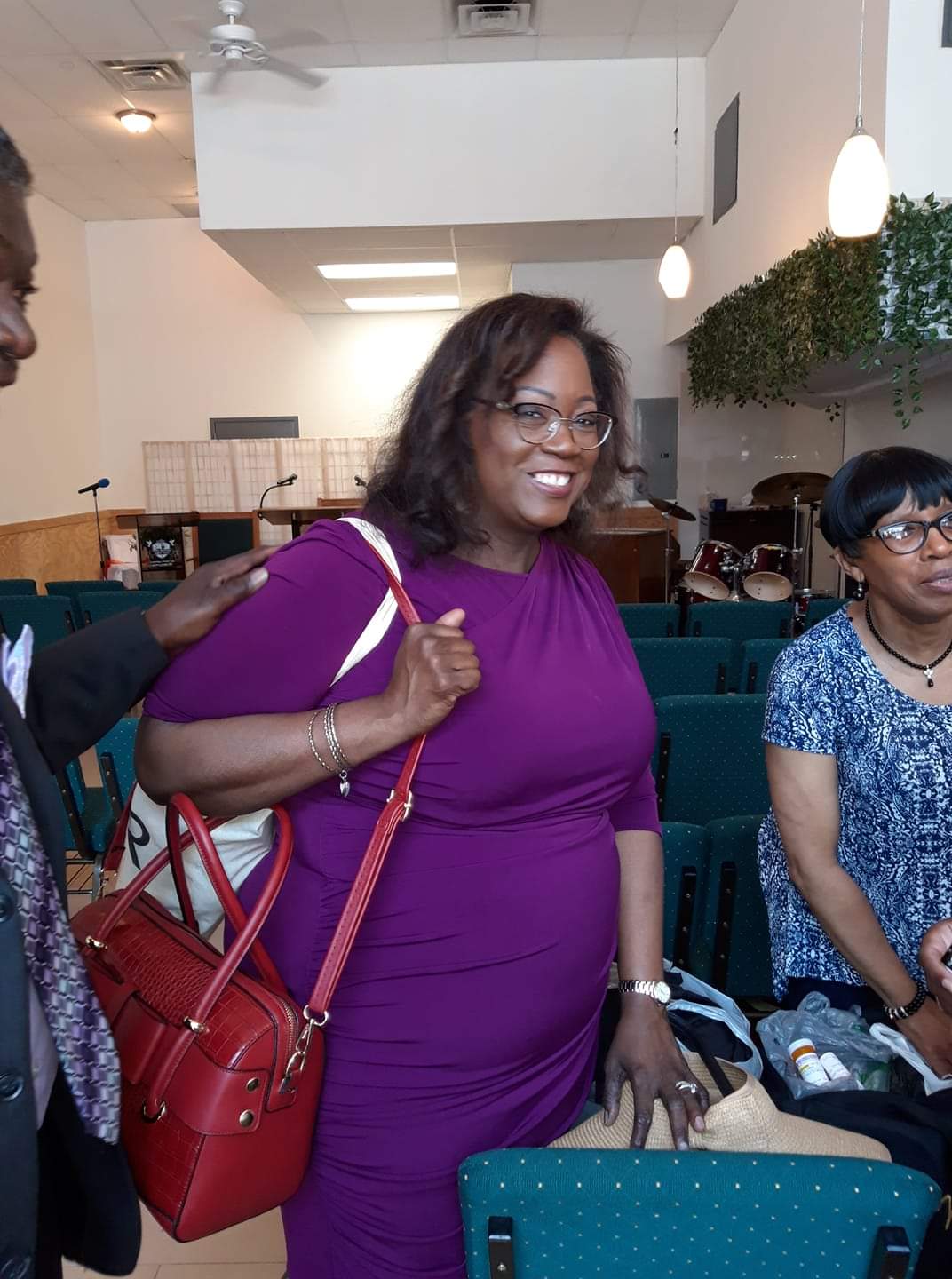 a woman in a purple dress is holding a red purse