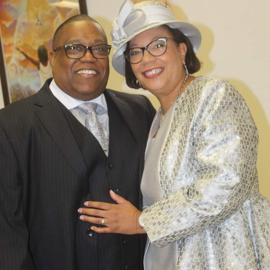a man in a suit and tie and a woman in a hat are posing for a picture