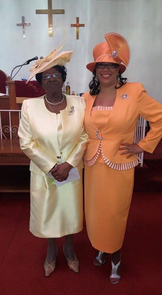 two women in yellow dresses and orange hats are standing next to each other in a church .
