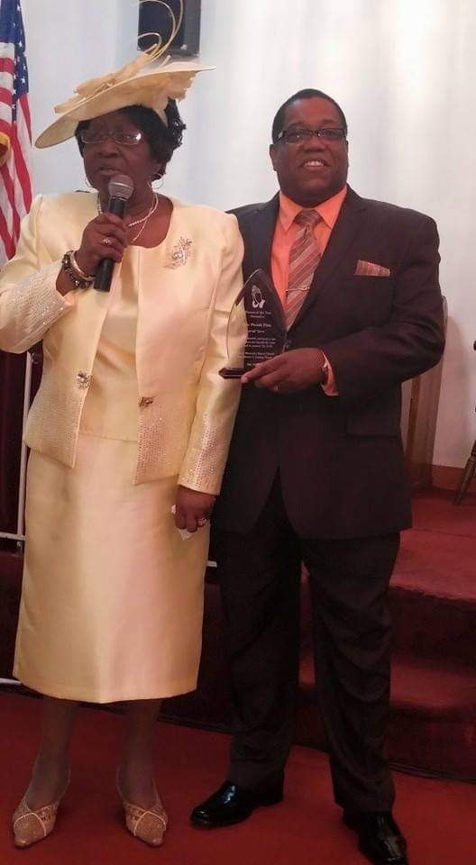 a woman in a yellow dress is standing next to a man in a suit holding a trophy .