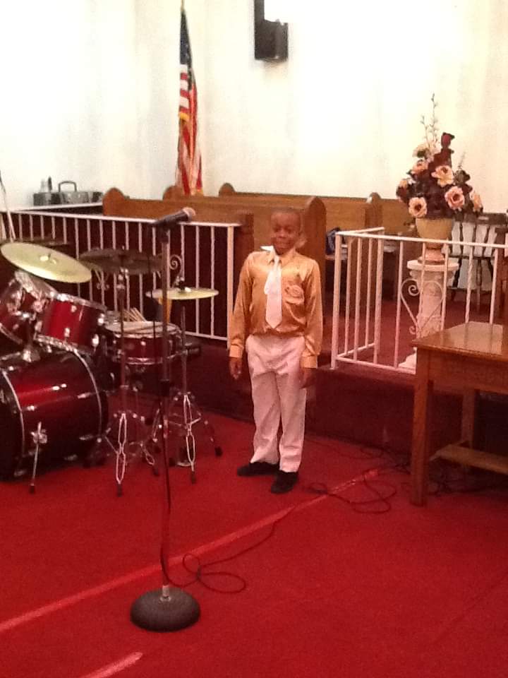 a young boy stands in front of a microphone in a church