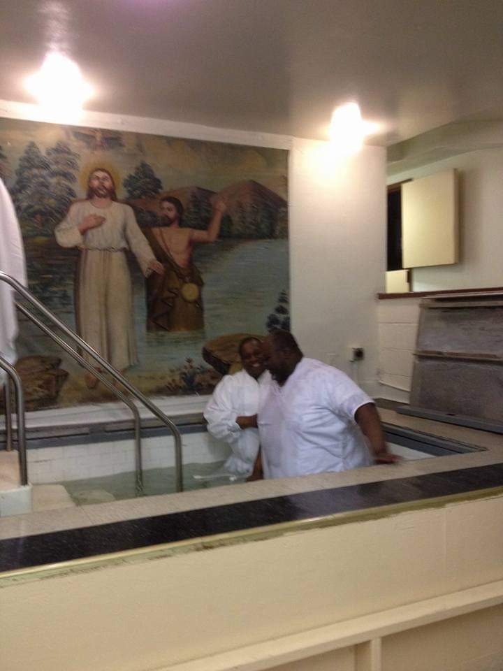 a man is standing in a bathtub with a painting of jesus on the wall behind him .