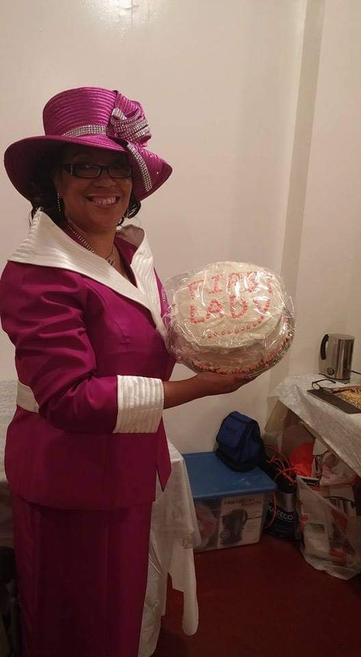 a woman in a purple hat is holding a cake .